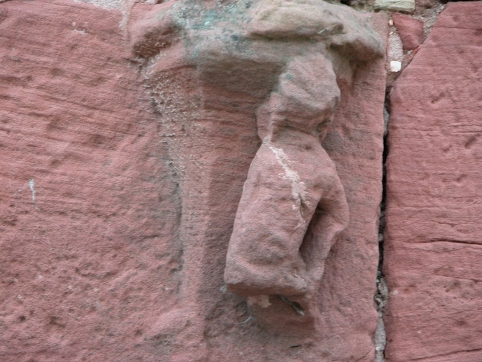 Sculpture très endommagée en grès rouge située à gauche de la porte d'entrée, représentant sans doute un homme chevauchant un dauphin.
