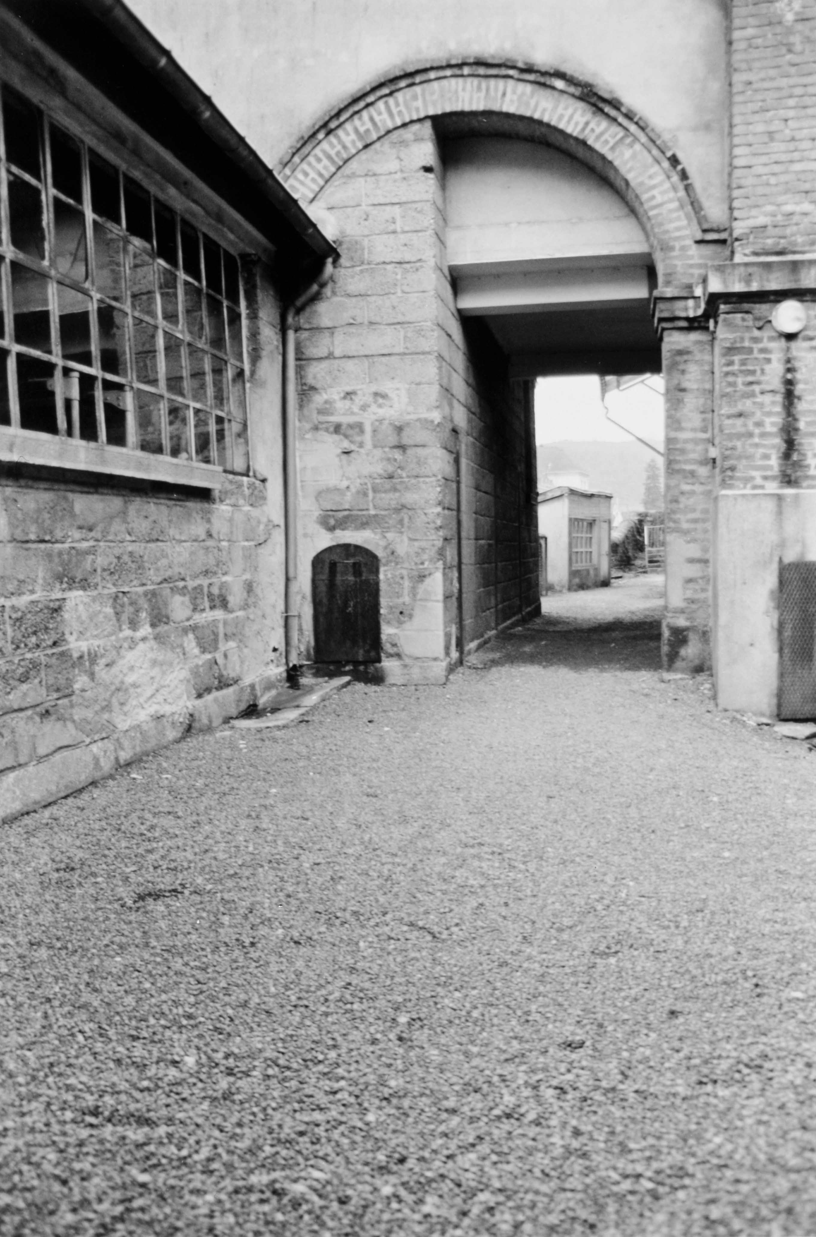 Le passage couvert menant de la teinturerie à l'arrière du bâtiment des ateliers de tissage. Il est orné d'un arc plein-cintre en briques à extrados brisé (reportage photographique de L. Yeghicheyan, 1992, Aubusson, Musée départemental de la Tapisserie)