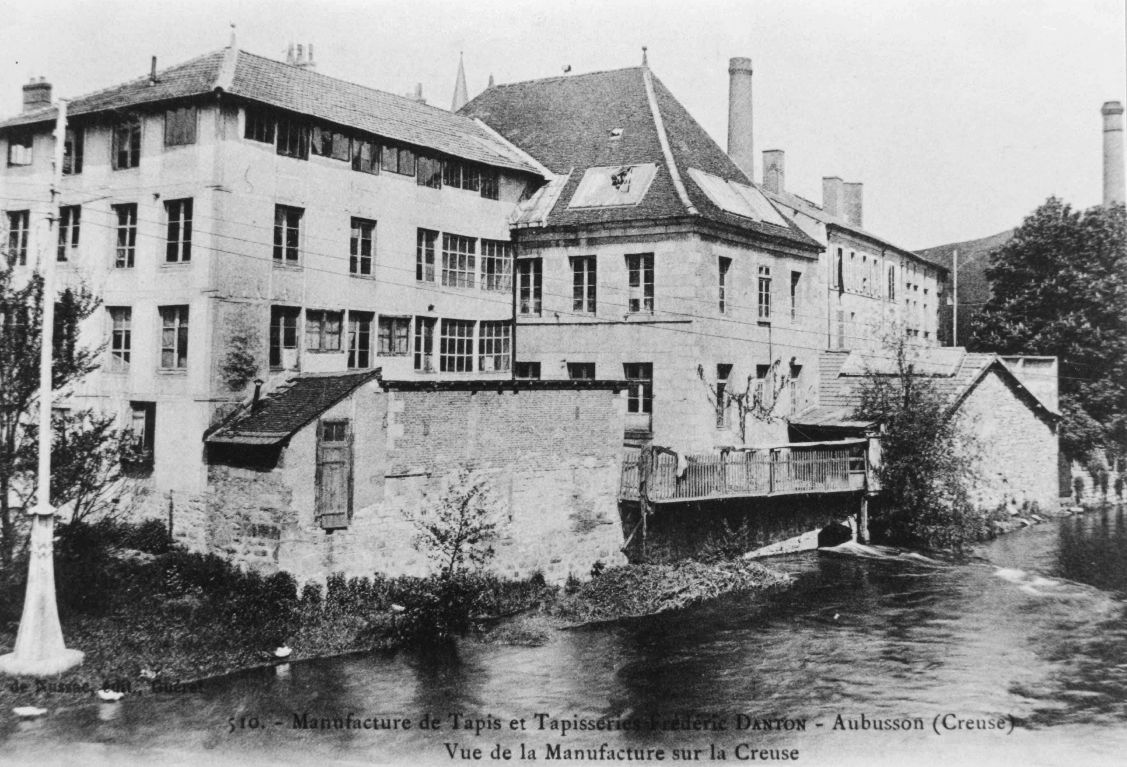Carte postale de la manufacture Danton dans le 1er quart du 20e siècle : les bâtiments, vus depuis le Pont Neuf, en direction de l'est, sur la rive droite de la Creuse. 