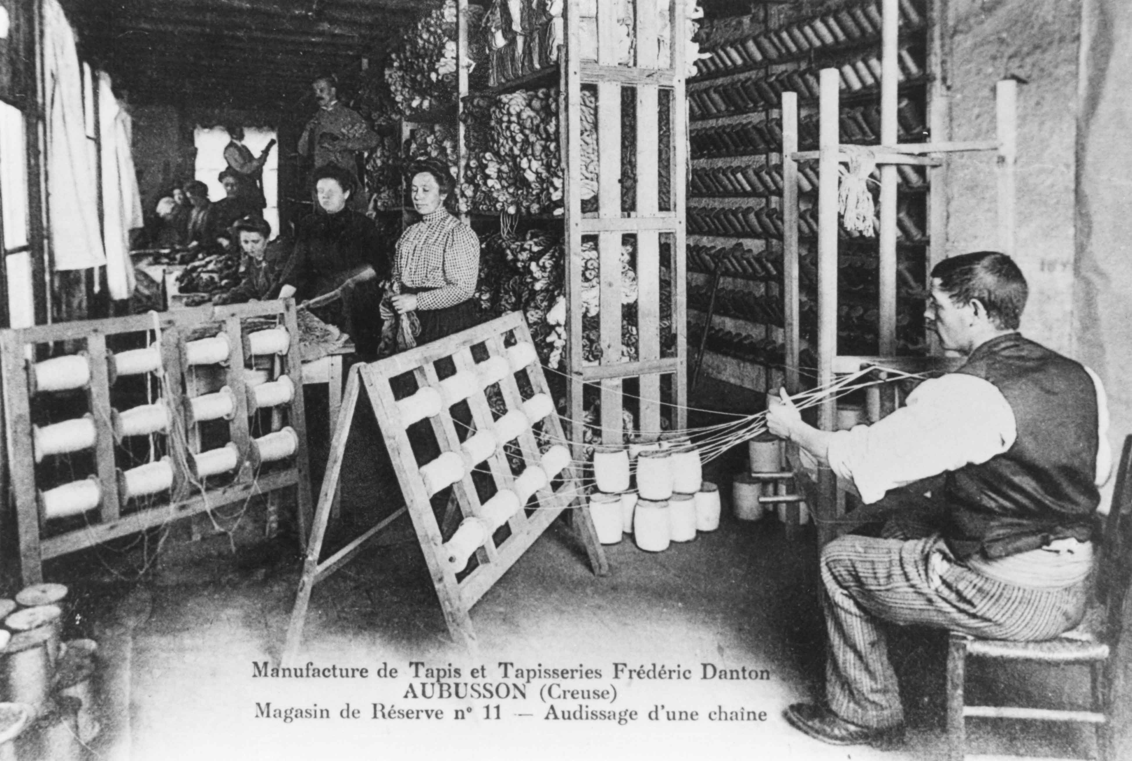 Carte postale (1er quart du 20e siècle) : l'ourdissage d'une chaîne dans le magasin de réserve n° 11 de la manufacture (Aubusson, centre de documentation du Musée départemental de la Tapisserie)