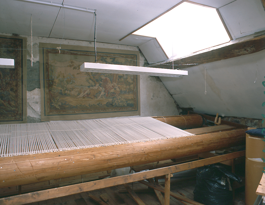 Un métier à tisser de basse lisse, installé au second étage de la manufacture, avec la chaîne mise en tension entre les deux ensouples de bois.