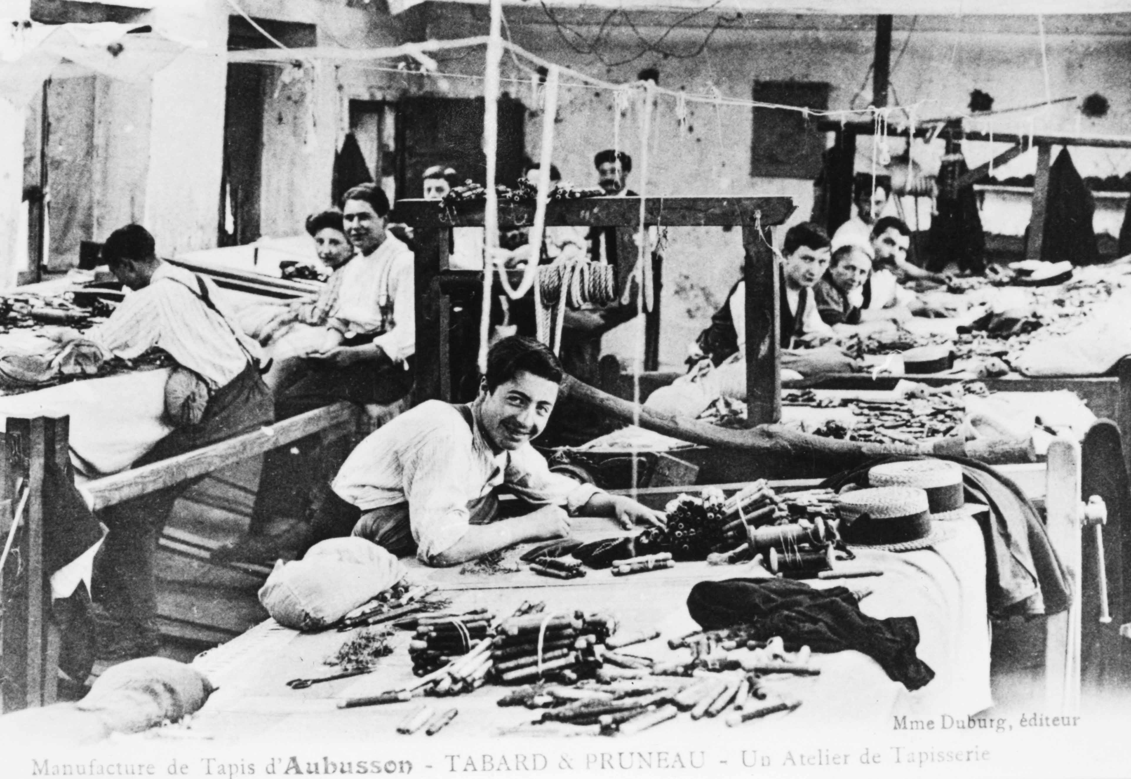 Carte postale (1er quart du 20e siècle) d'un atelier de tapisserie de la manufacture Tabard et Pruneau, avec les ouvriers au travail (Aubusson, centre de documentation du Musée départemental de la Tapisserie)