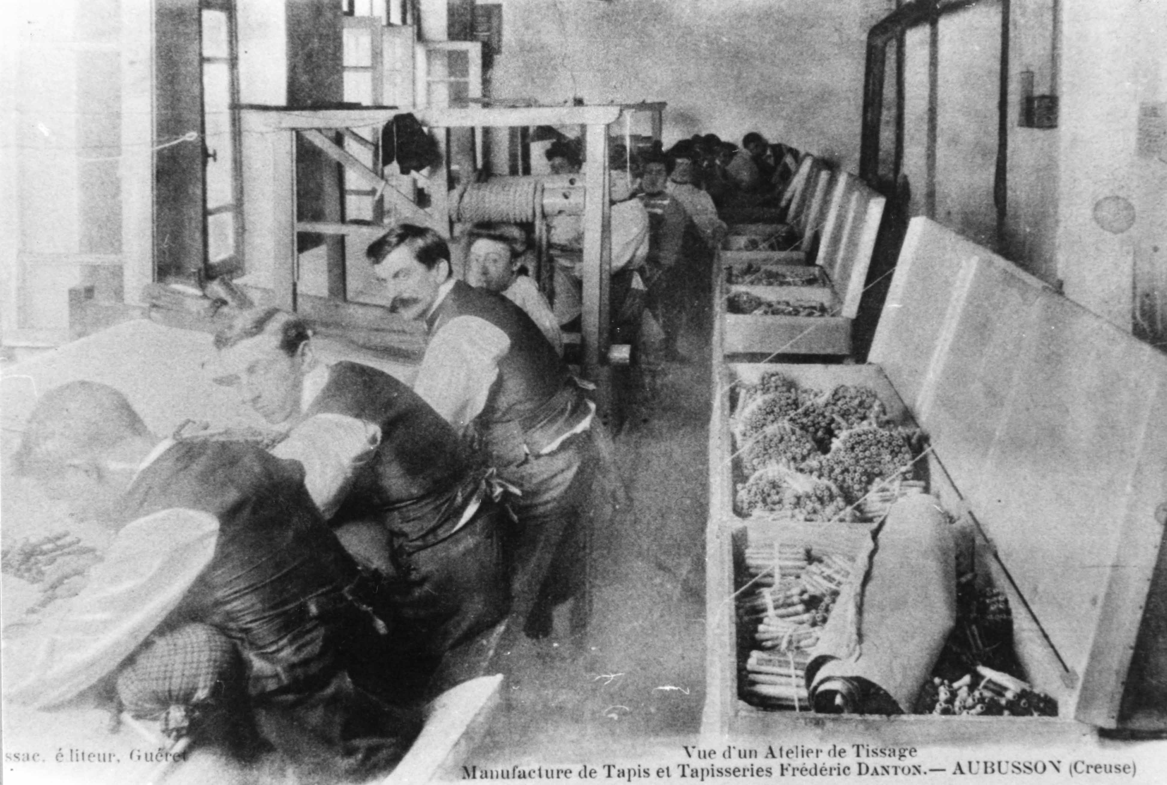 Carte postale (1er quart 20e siècle) : un atelier de tissage de la manufacture Danton, avec les ouvriers au travail (Aubusson, centre de documentation du Musée départemental de la Tapisserie)