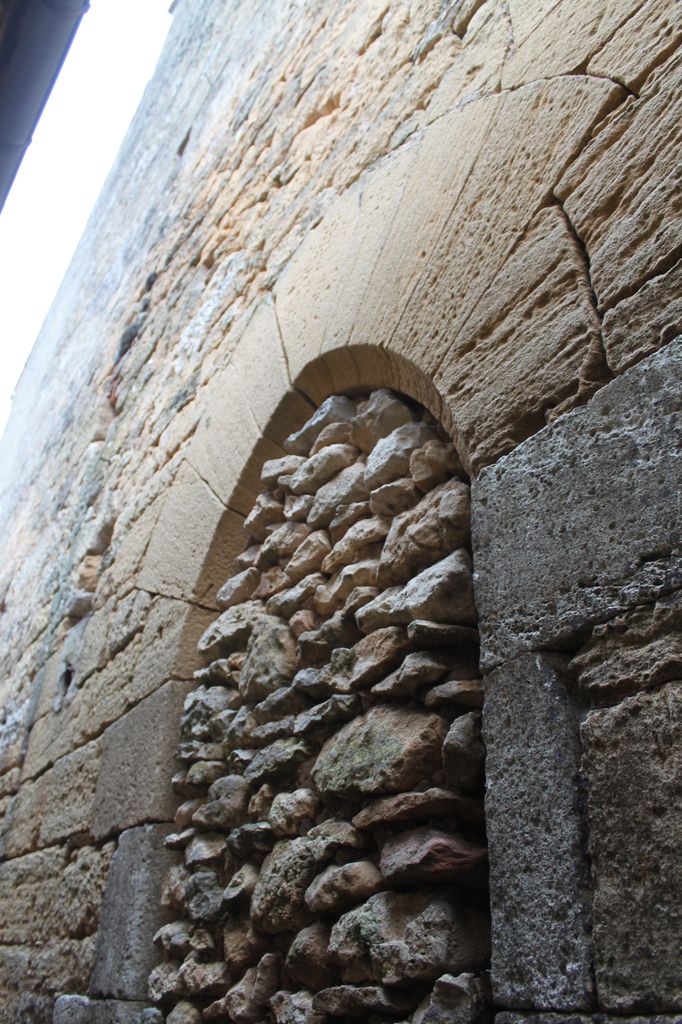 Vue d'une porte à longs claveaux (XIVe ou XVe) murée au côté nord du corps de logis principal.