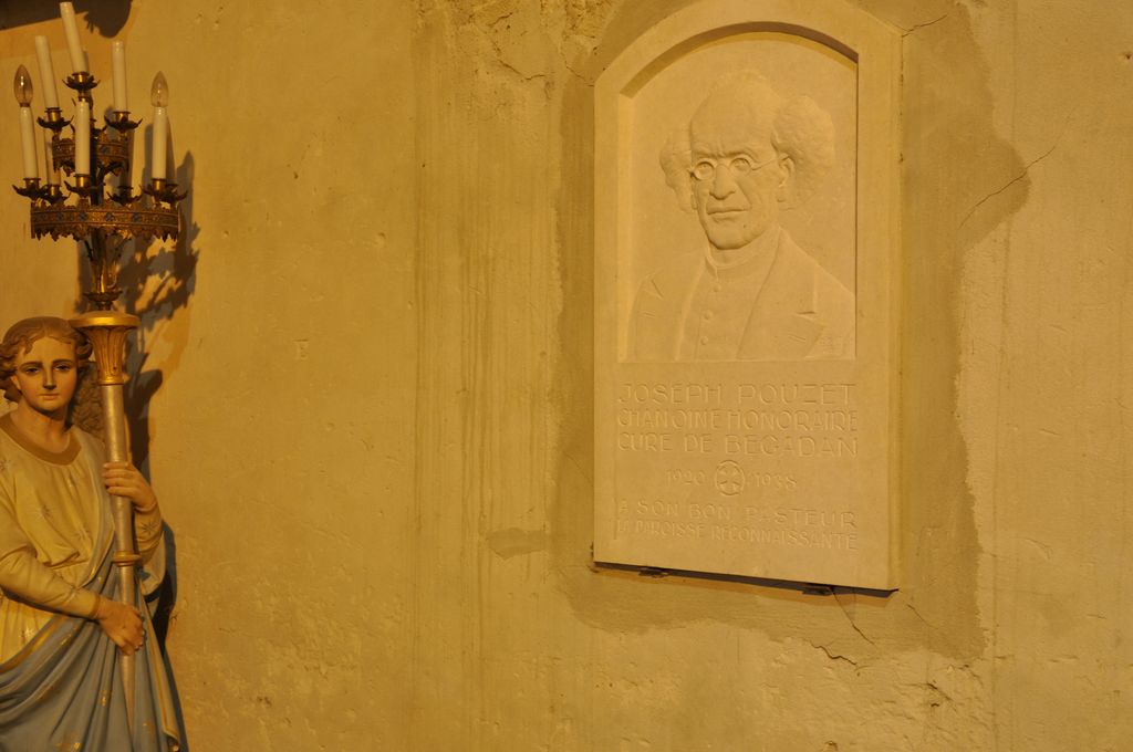 Bas-côté sud : plaque commémorative portant l’inscription : JOSEPH POUZET / CHANOINE HONORAIRE / CURE DE BEGADAN / 1920-1938 / A SON BON PASTEUR / LA PAROISSE RECONNAISSANTE.