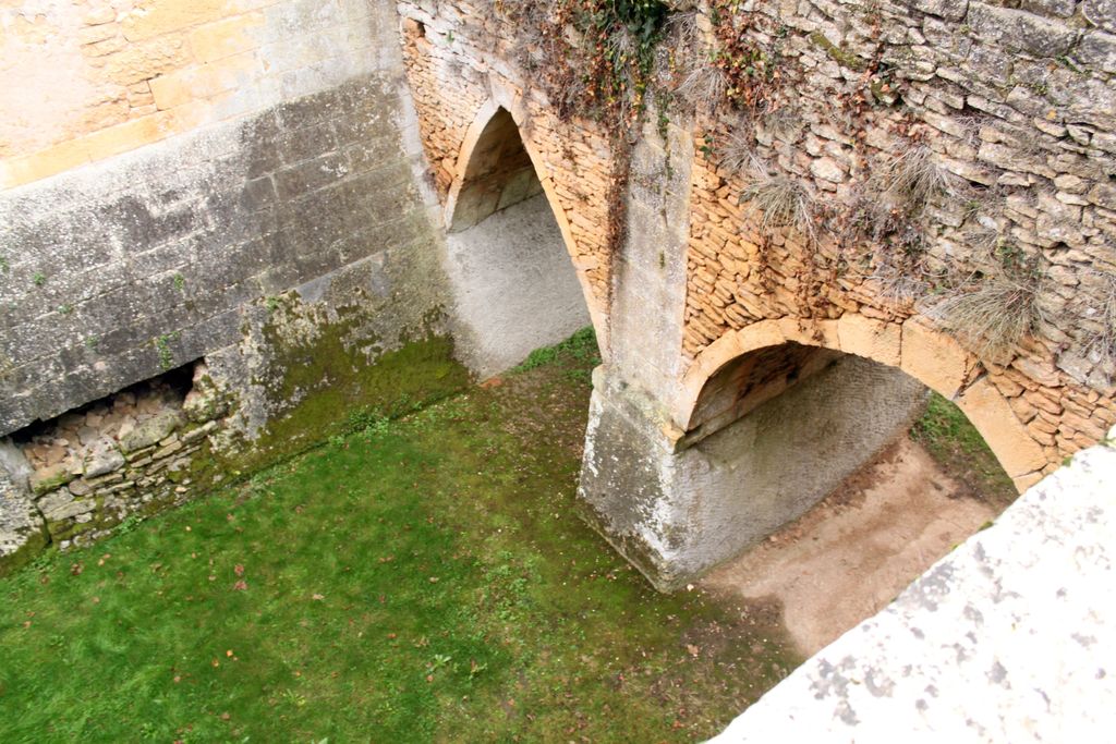 Vue plongeante sur le pont dormant en pierre avec son pilier central en pierre de taille ; rocher taillé en partie inférieure du pilier central et de l'escarpe ; douves sèches.