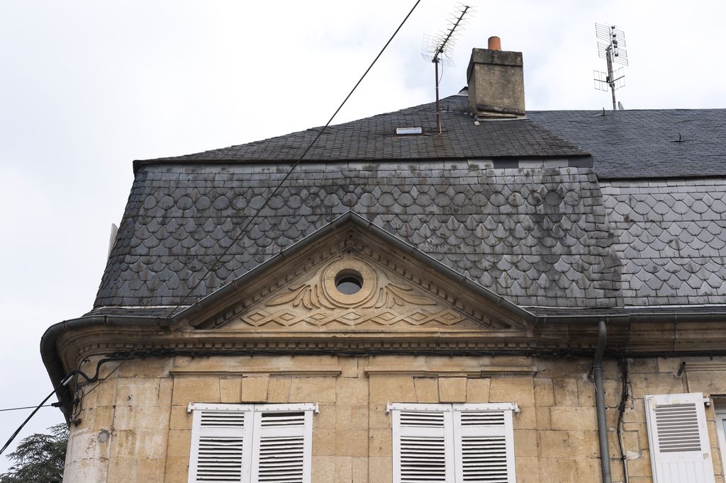 Détail d'un fronton triangulaire percé d'un oculus et d'un toit à brisis couvert d'ardoises taillées d'une maison du XIXe siècle de Montignac.