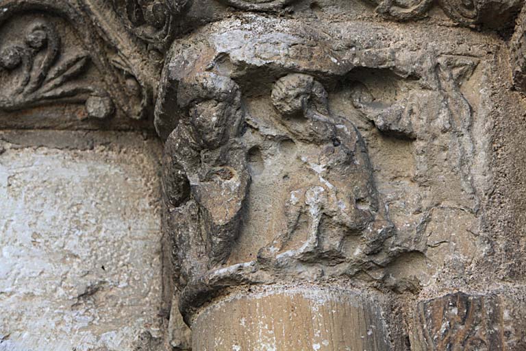 Façade occidentale, premier niveau, arcature sud, piédroit droit, vu de trois quarts. Chapiteau interne : scène, personnage auréolé penché en avant face à un personnage assis.
