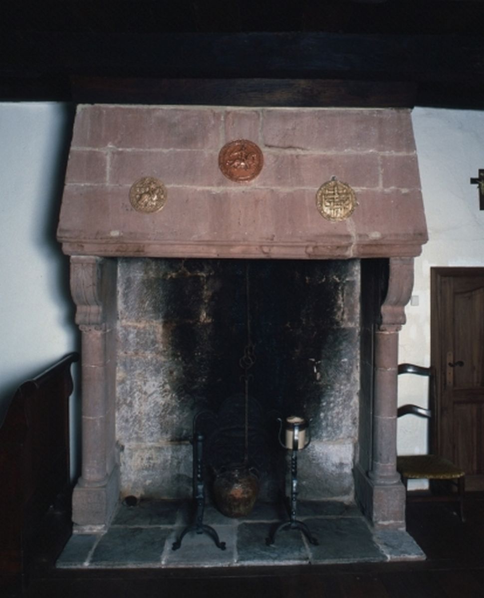 Cheminée adossée en grès rouge avec une hotte droite, présentant des piédroits en forme de fût de colonne.
