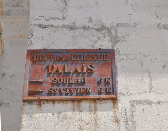Plaque d'indication routière fixée sur la façade d'une maison : distances jusqu'à Saint-Vivien-de-Médoc et jusqu'à Soulac.