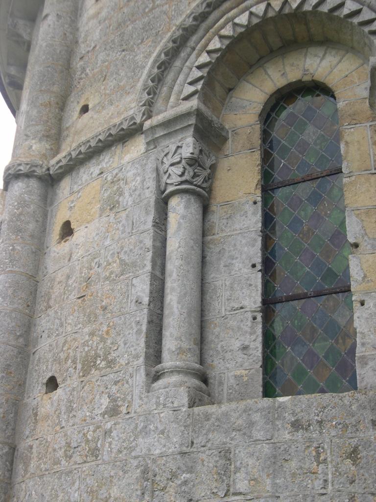 Chevet, abside, élévation nord, fenêtre, colonnette gauche à base moulurée, chapiteau à décor végétal et masque. Vue de trois quarts.