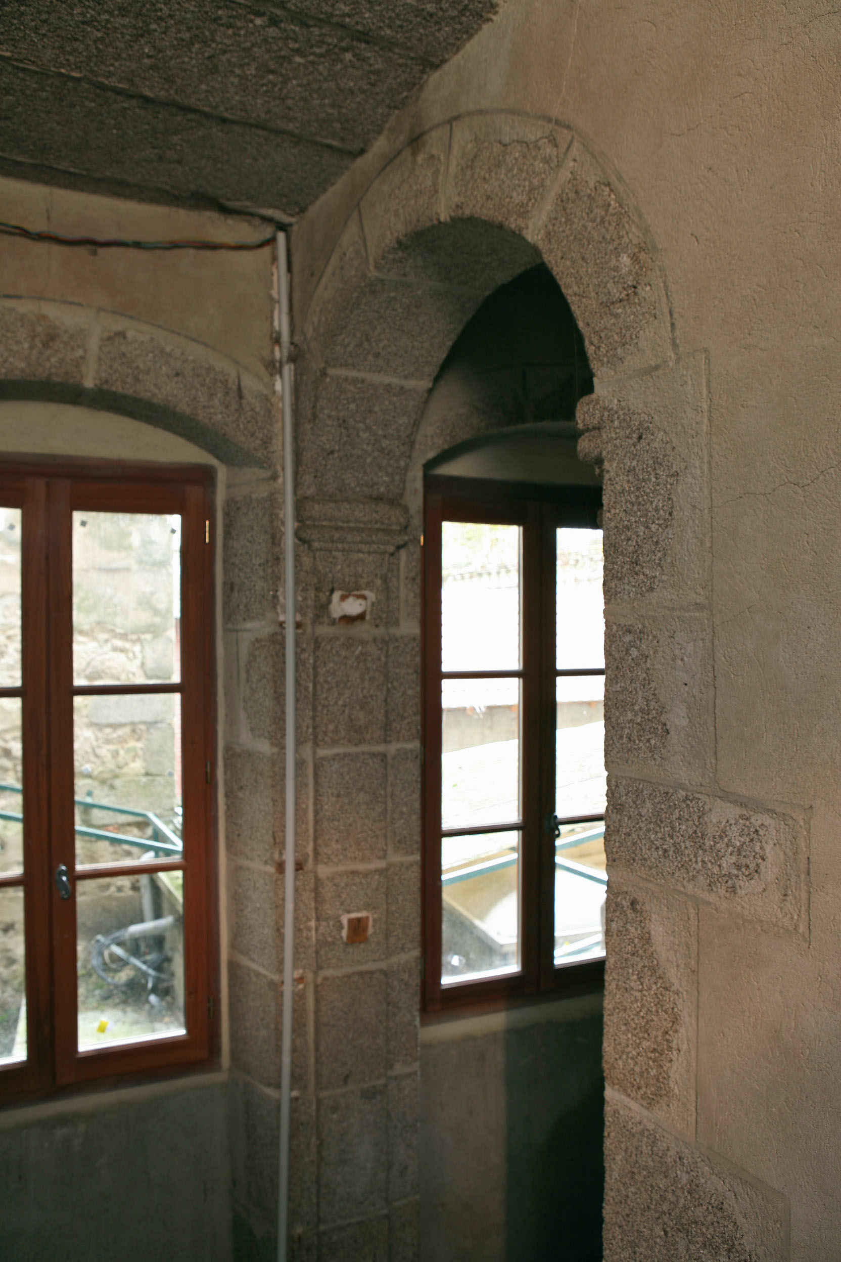 Intérieur de la tour hors-œuvre. Vue partielle, depuis le premier étage, montrant la cage d'escalier en pierre, à volées droites et le mur-noyau, percé d'une ouverture en plein cintre au niveau du repos. 