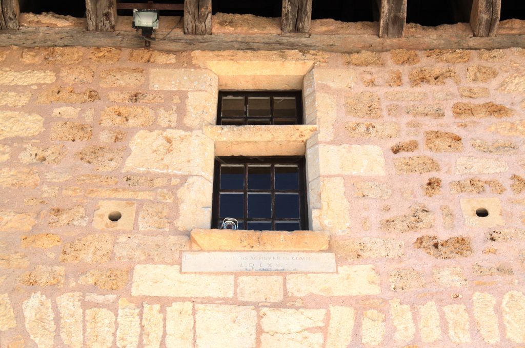 Détail de la fenêtre (demi-croisée) au premier étage du pavillon d'entrée, au-dessus du passage traversant côté cour : orifices de tir circulaires pour armes à feu légères encadrant une table portant une inscription en caractères romains dans l'allège de la fenêtre : 