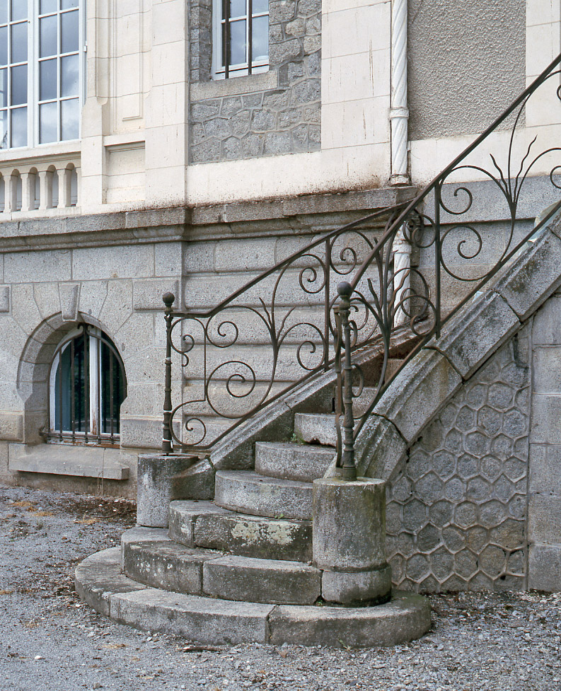 Façade postérieure : détail de l'escalier extérieur tournant, en maçonnerie, avec sa rampe en fer forgé décorée de motifs floraux. 