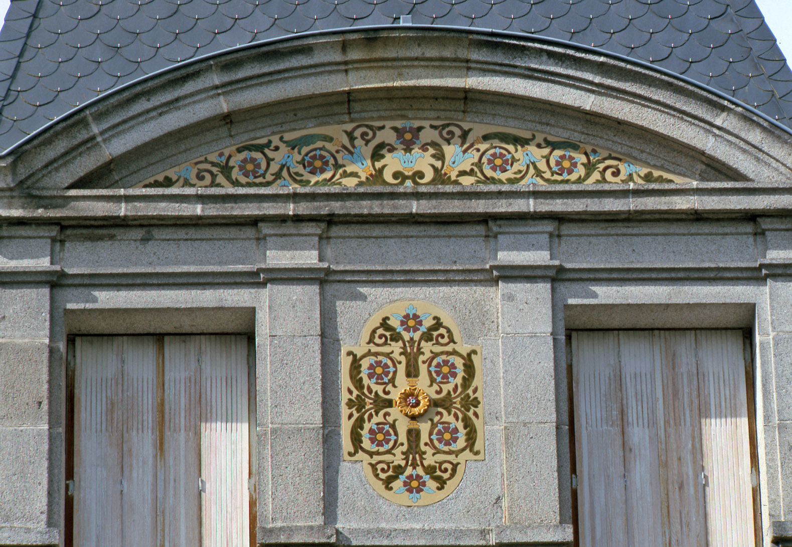 Détail du fronton cintré décoré de céramique moulée polychrome. 