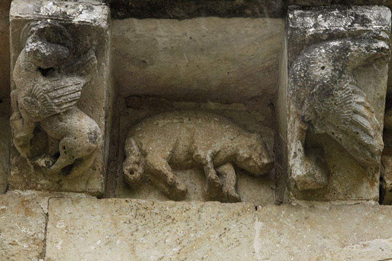 Élévation sud, troisième travée, corniche à modillons et métopes ornés au-dessus du portail, modillon 1 (taureau ailé de saint Luc), métope 2 (cochon), modillon 2 (aigle de saint Jean).