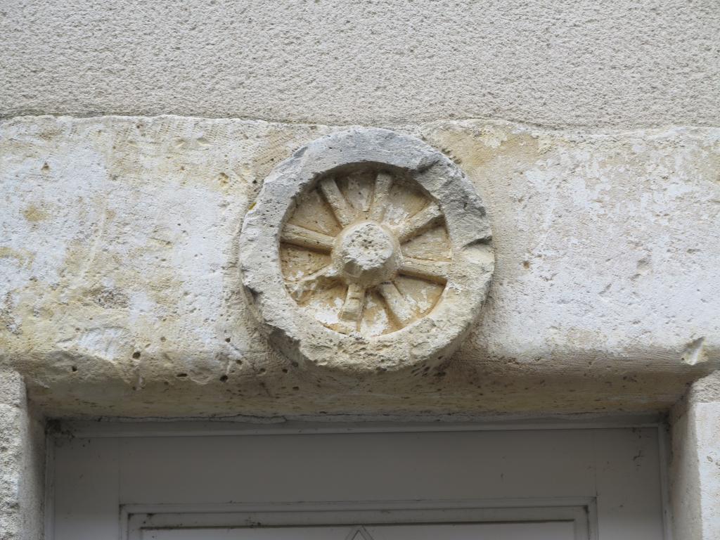 Linteau de la porte, arrondi et orné d'une roue de charrette, en remploi (n° 16 rue du Carroir). Linteau de la porte, arrondi et orné d'une roue de charrette, en remploi (n° 16 rue du Carroir).