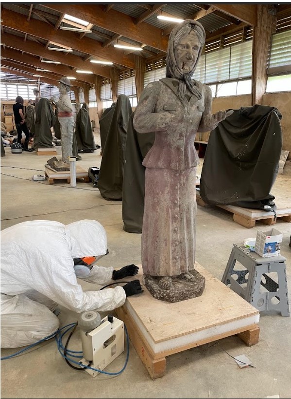 Elimination des dépôts par la projection de particules abrasives sur la surface de la statue de la femme au foulard.