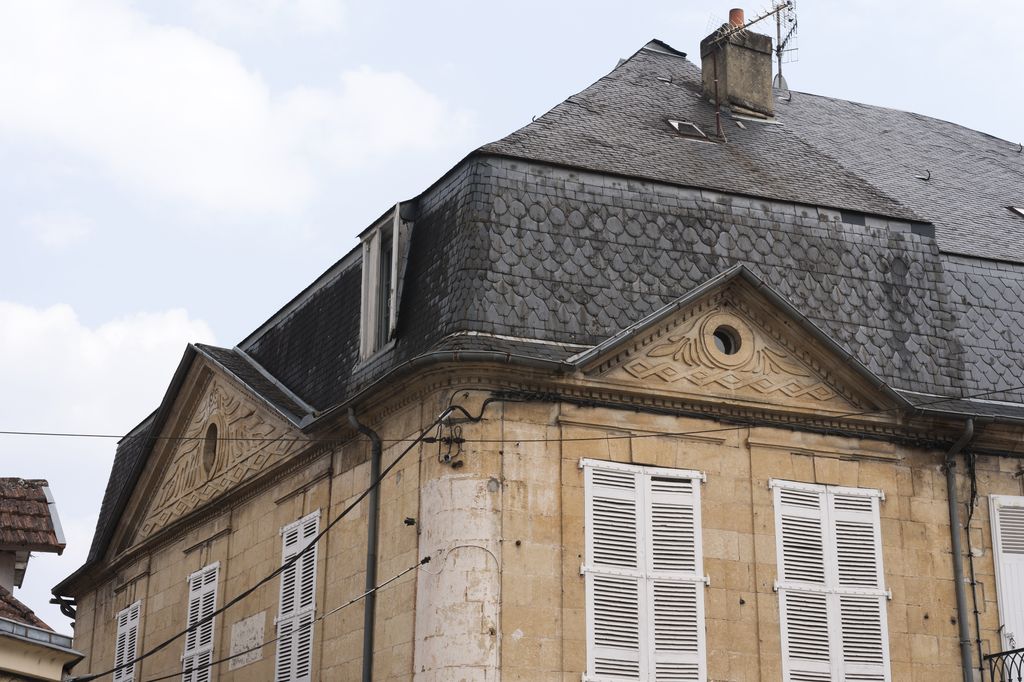 Détail de frontons triangulaires, d'un toit à brisis couvert d'ardoises taillées et de l'angle adouci (avec corniche continue) des façades sur rue d'une maison du XIXe siècle de Montignac.