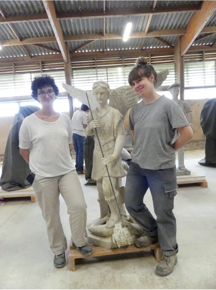 Sculpture de saint Michel terrassant le démon après la première semaine de chantier, encadrée par les deux étudiantes chargées de sa restauration.