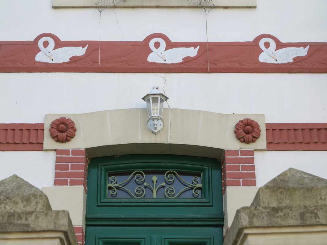 Détail du décor de la façade : frise de cygnes, fleurs et bandeau en terre cuite, alternance de pierre et de brique.