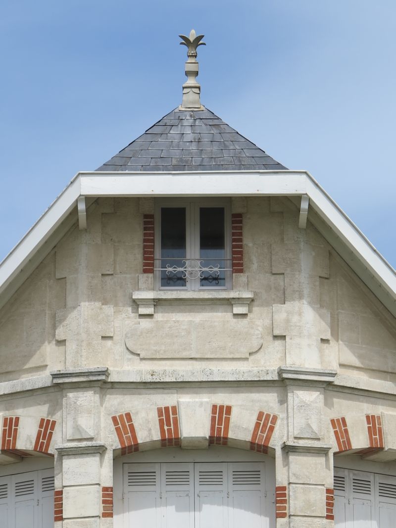 Détail du pignon : décor en brique, demi-croupe de toit, épi.
